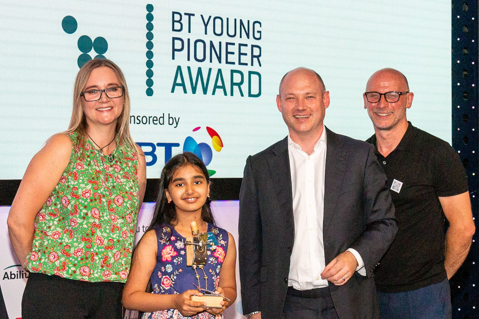 Kate Russell, Mihika Sharma (9), Andy Wales BT and Mark Walker on stage holding the BT Young Pioneer Award