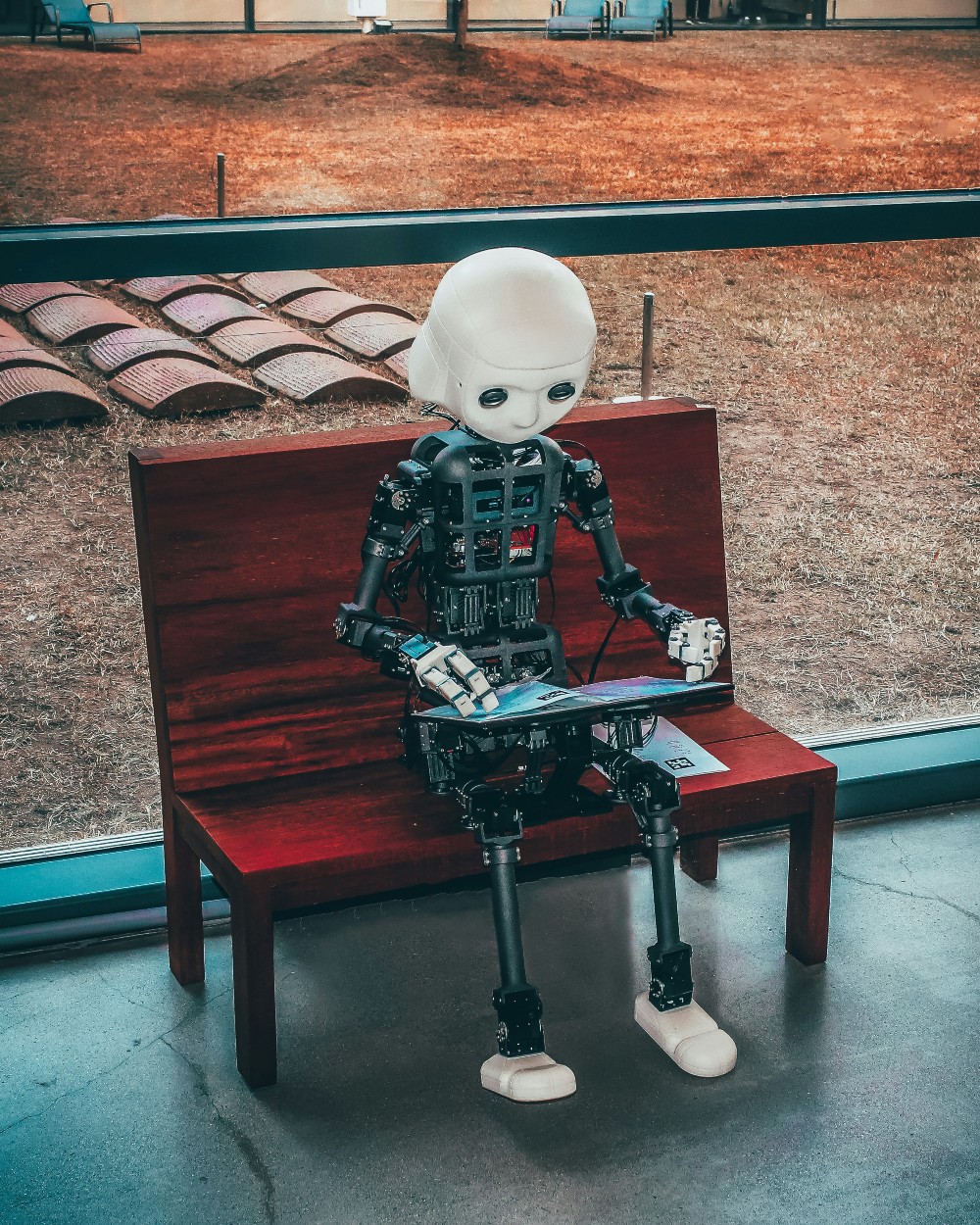 A robot sits on a bench with a laptop