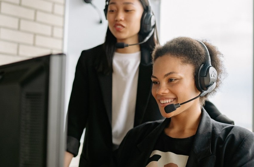Two women in the workplace call centre, one on phone smiling, one standing behind smiling