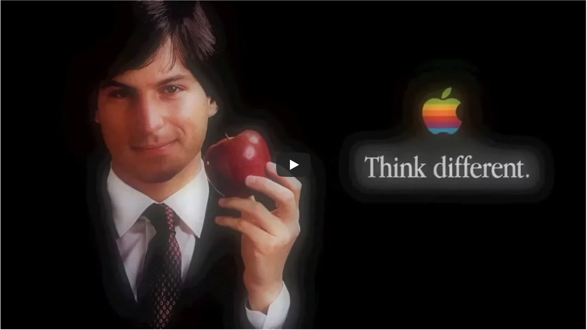 Image shows a man in a suit holding an Apple. Behind him is the Apple logo and the slogan 'think difefrent'