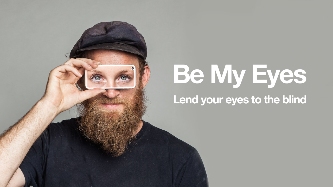 Photo of a man holding up a smartphone to his eyes with an image of someone else's eyes on the phone display. Be My Eyes, lend your eyes to the blind strapline 