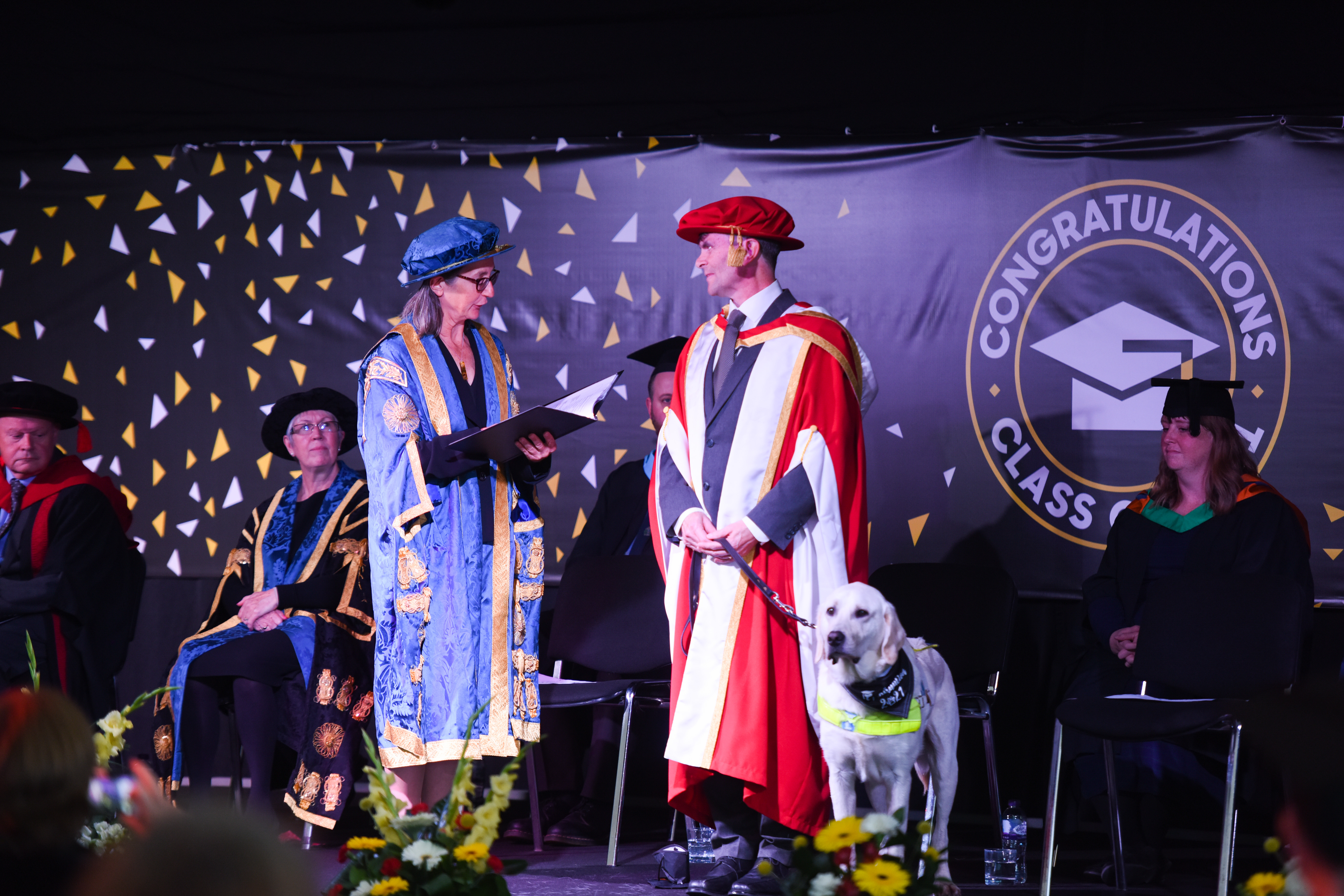 Chancellor of the University, Dr Helen Pankhurst awarding Robin Christopherson at the ceremony. Beside Robin stands his guide dog, Hugo.