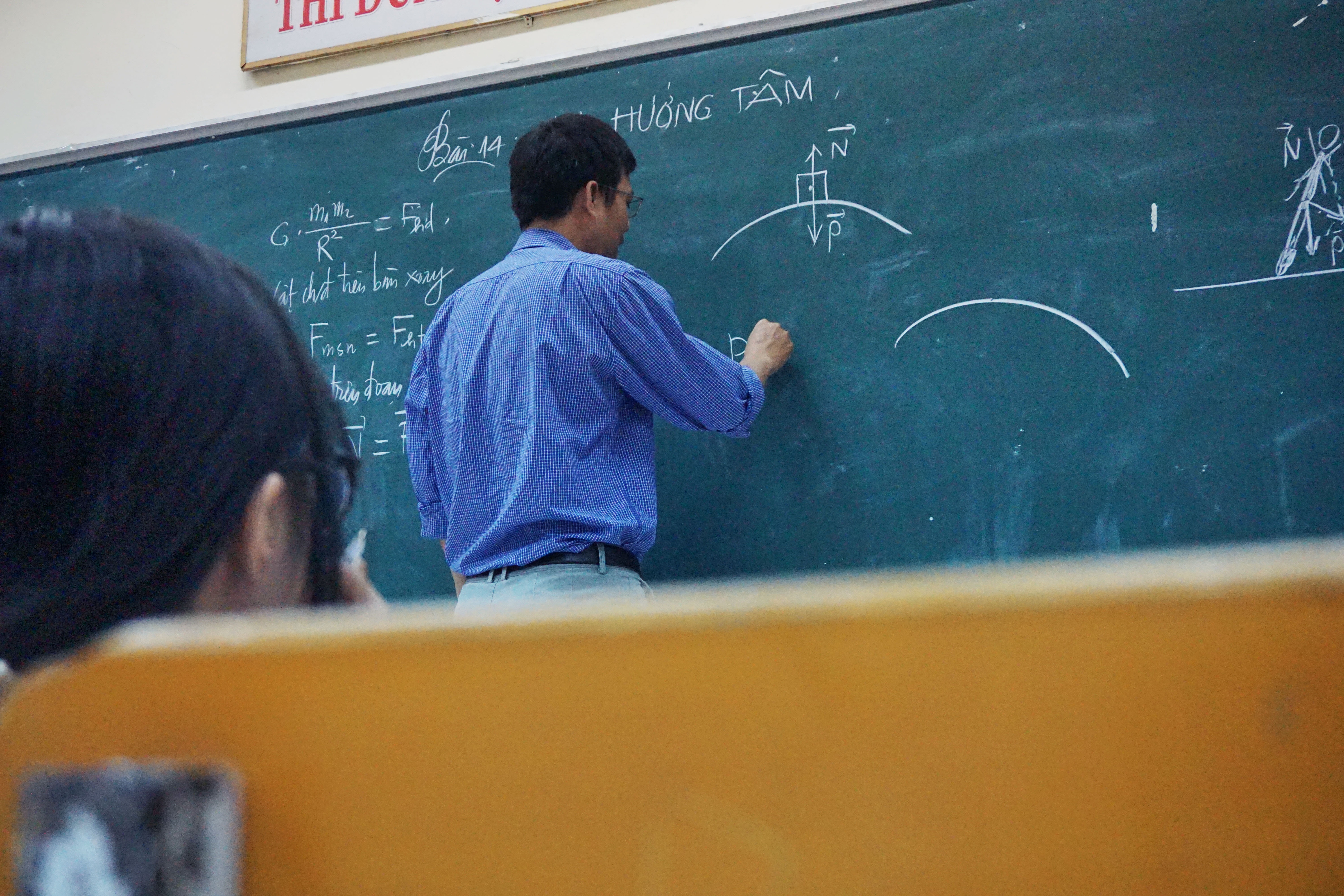 Male teacher stood with back to class writing on a blackboard