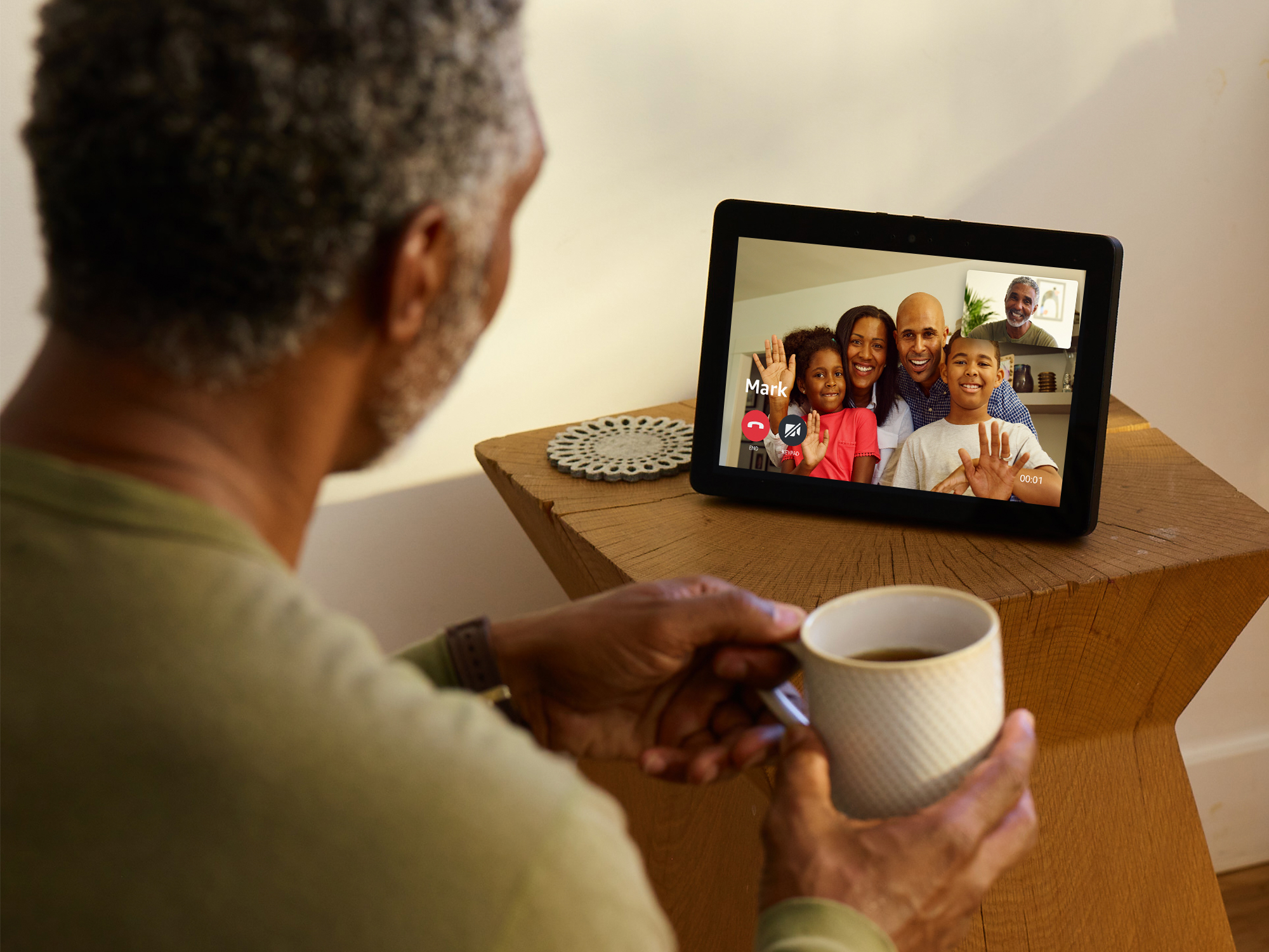 Image shows the Echo Show on a table with a group of people speaking and the back of the person talking to them
