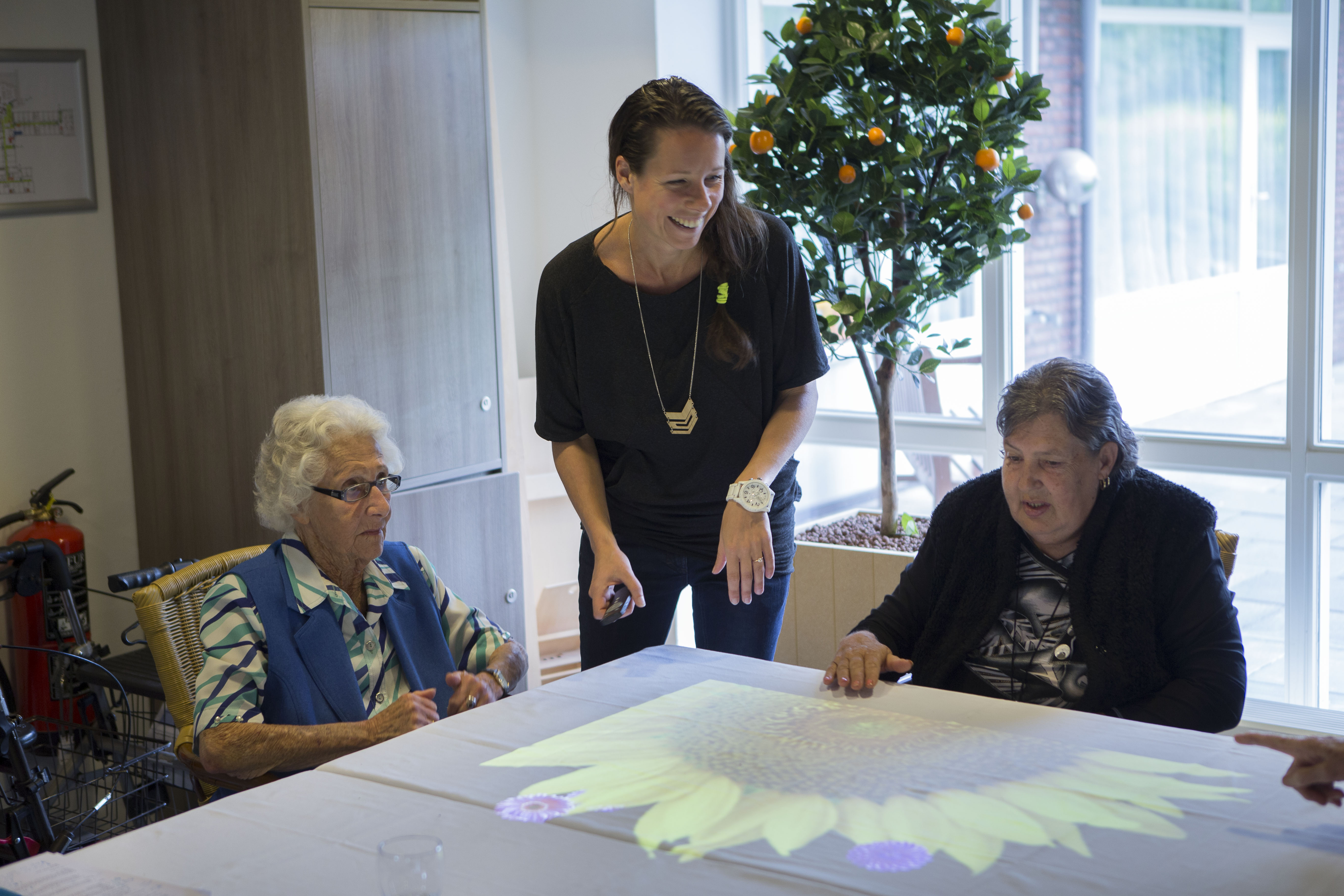 Images shows Tover CEO Hester Le Riche with some older people using the magic table. Images are projected onto the table.
