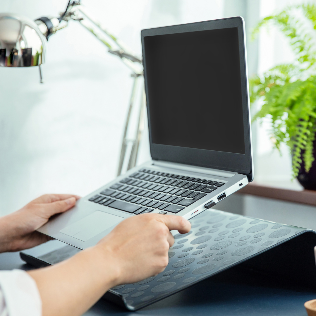A pair of hands placing a laptop onto a laptop stand. 