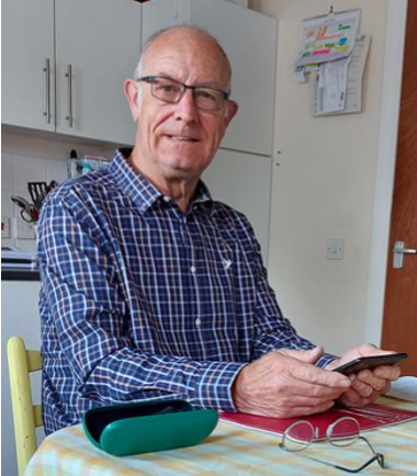 An old man sitting and holding a tablet in his hands. Smiling at the camera.