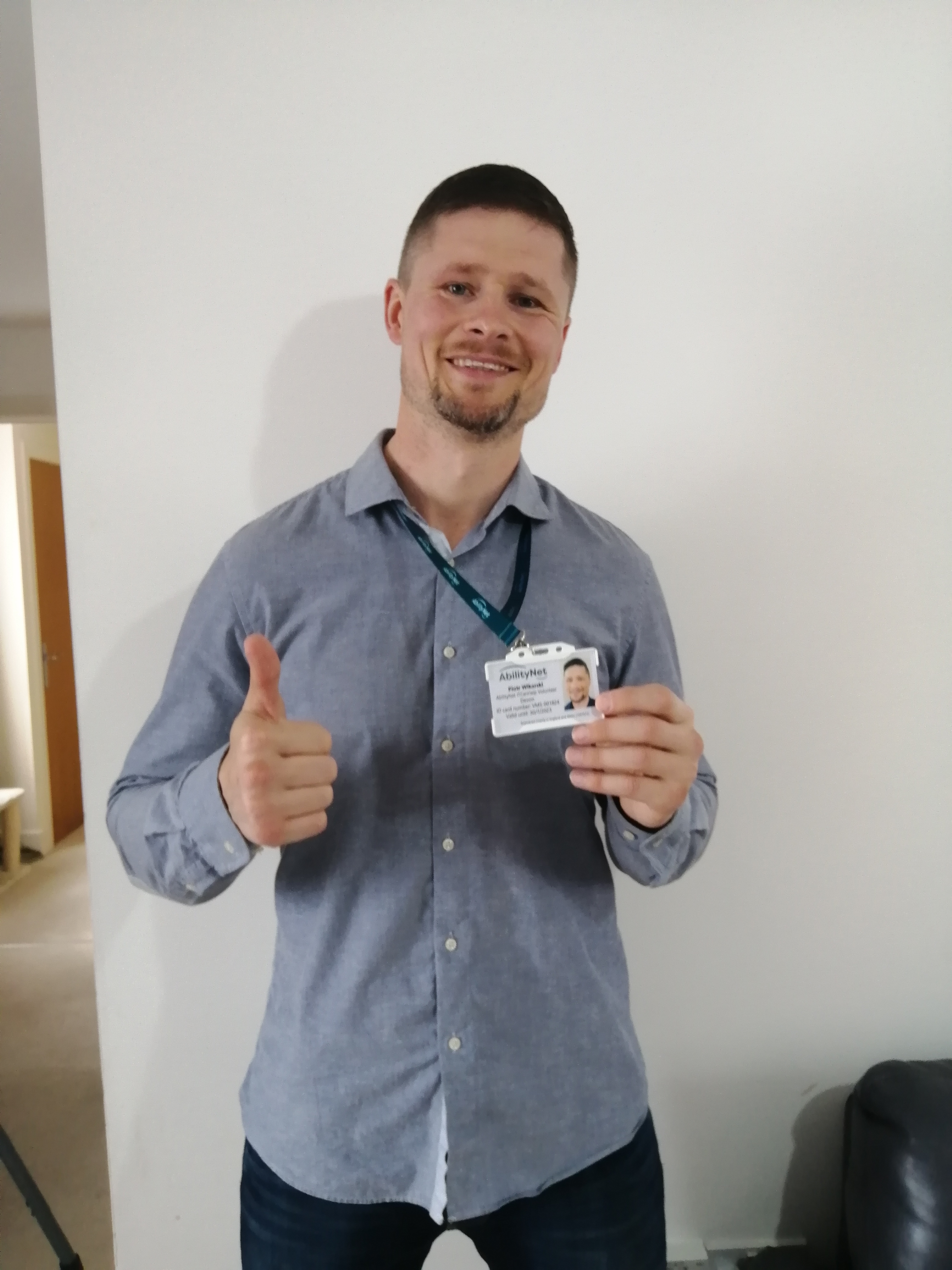 Image of Piotr holding his volunteers badge and giving camera a thumbs up. 