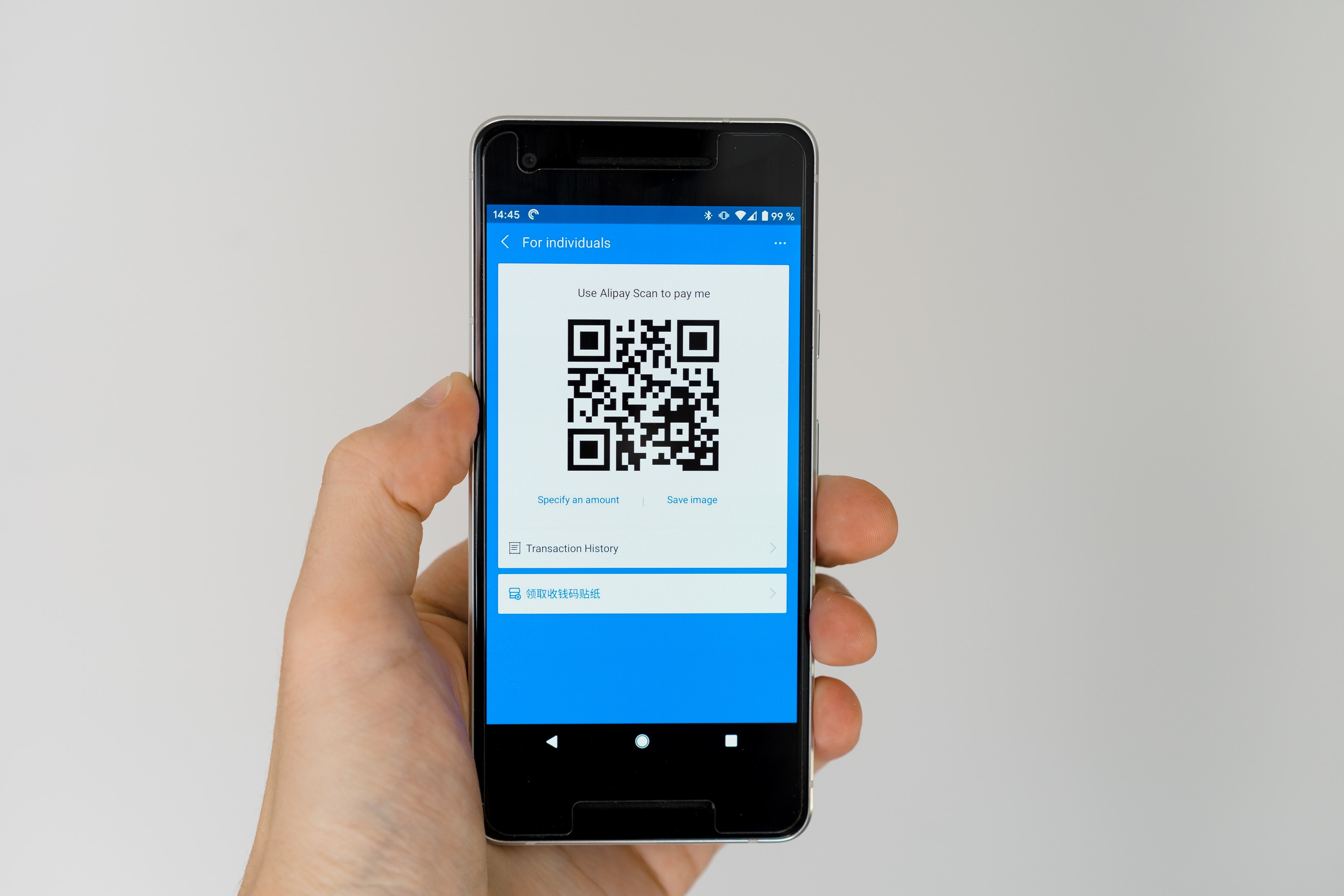 Image shows someone holding a mobile phone with a QR code the words 'transaction history' appear below the code