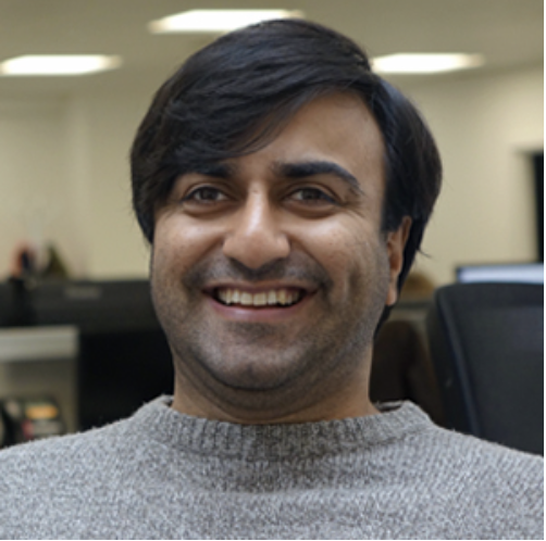 Adi Latif smiles face on into the camera with an office in the background