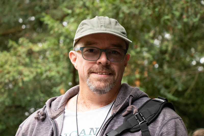 A picture of AbilityNet volunteer Shaun Bentley. He wears a cap and glasses