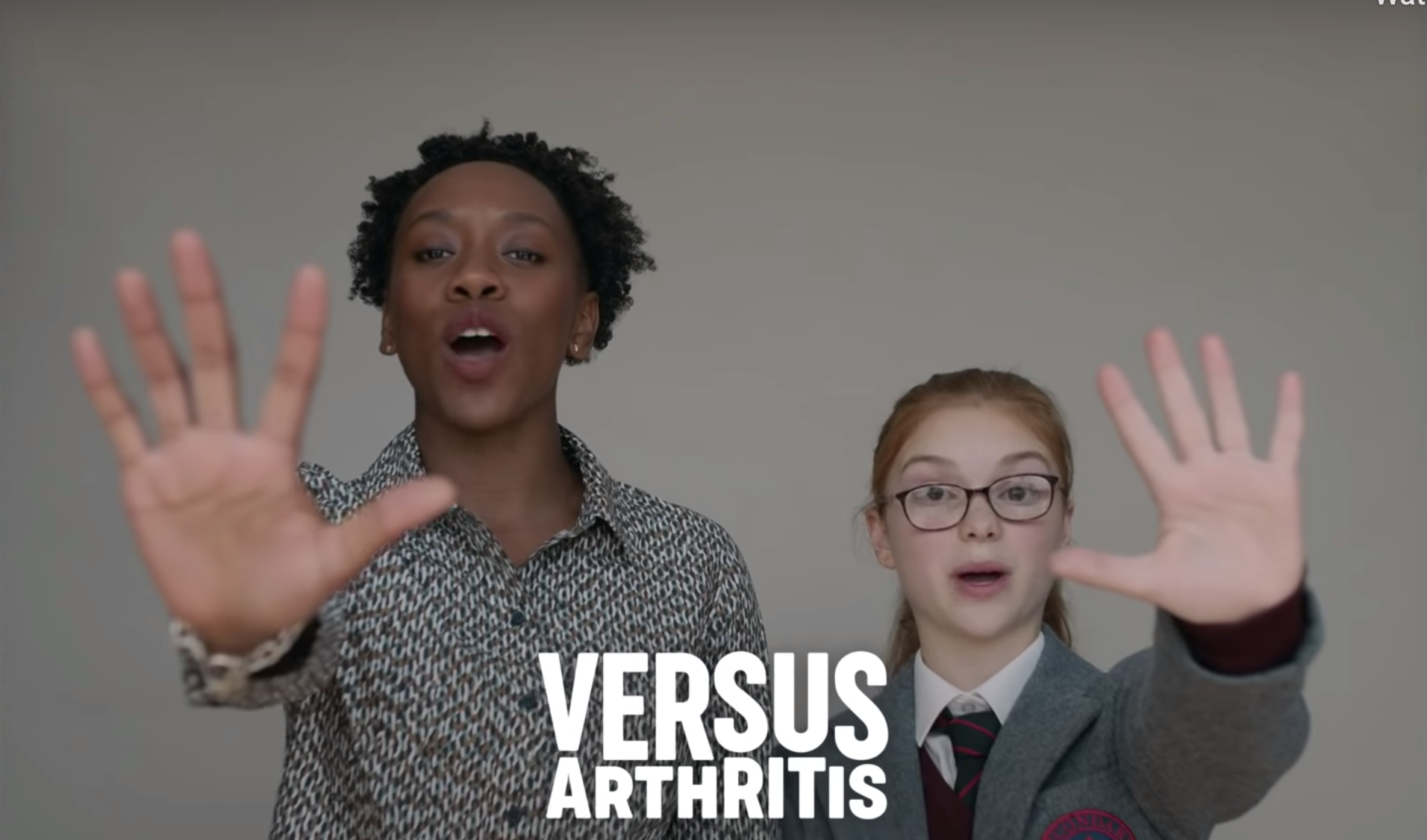 A teacher and pupil with hands outstretched with the word Versus Arthritis