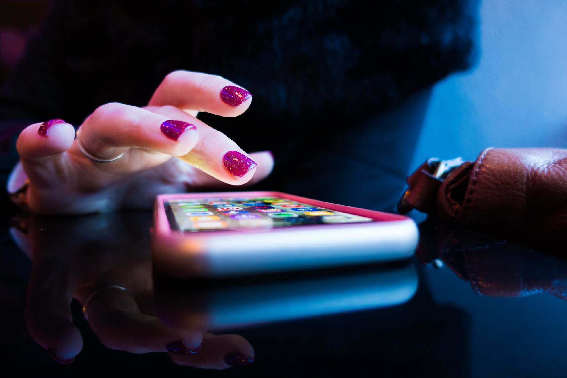 Womans hand poised over an iPhone with some apps showing. Her nails are decorated with glitter nail varnish.