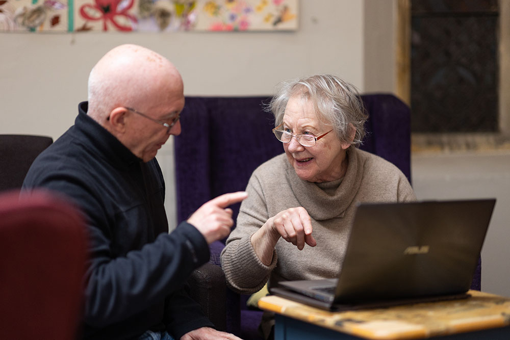 Older woman with grey hair and bald man sitting at computer chatting