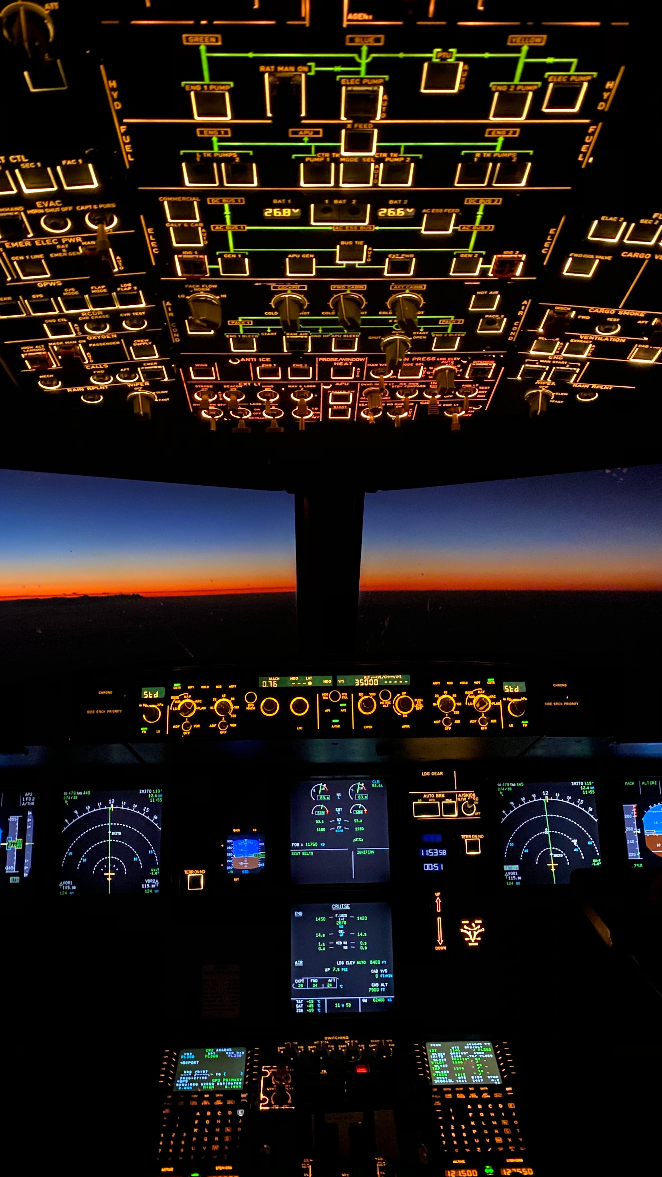 A picture of an airline cockpit. It is lit up and lots of dials and instructions