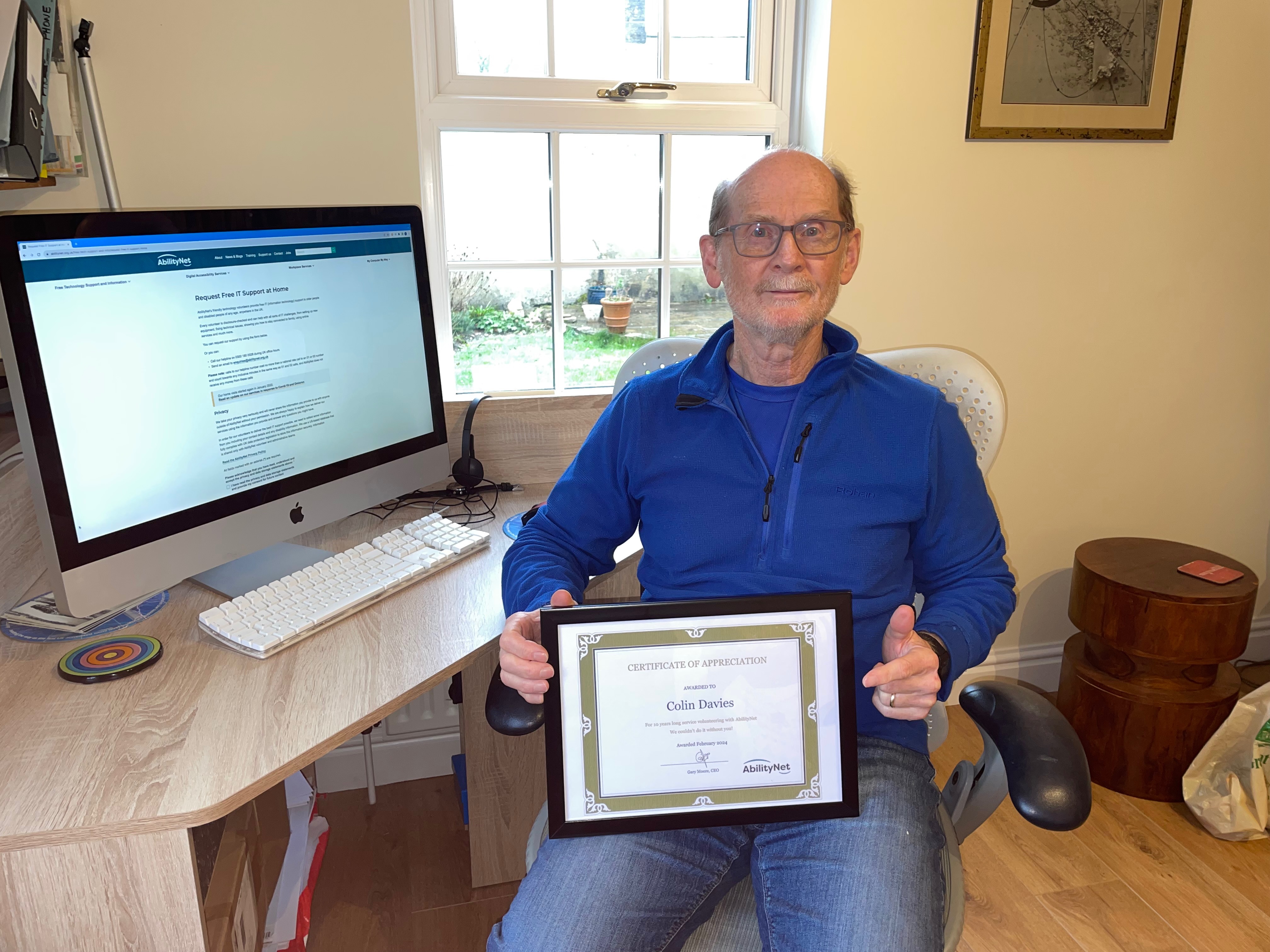 Colin Davies sitting at a desk holding a certificate for 10 years of service
