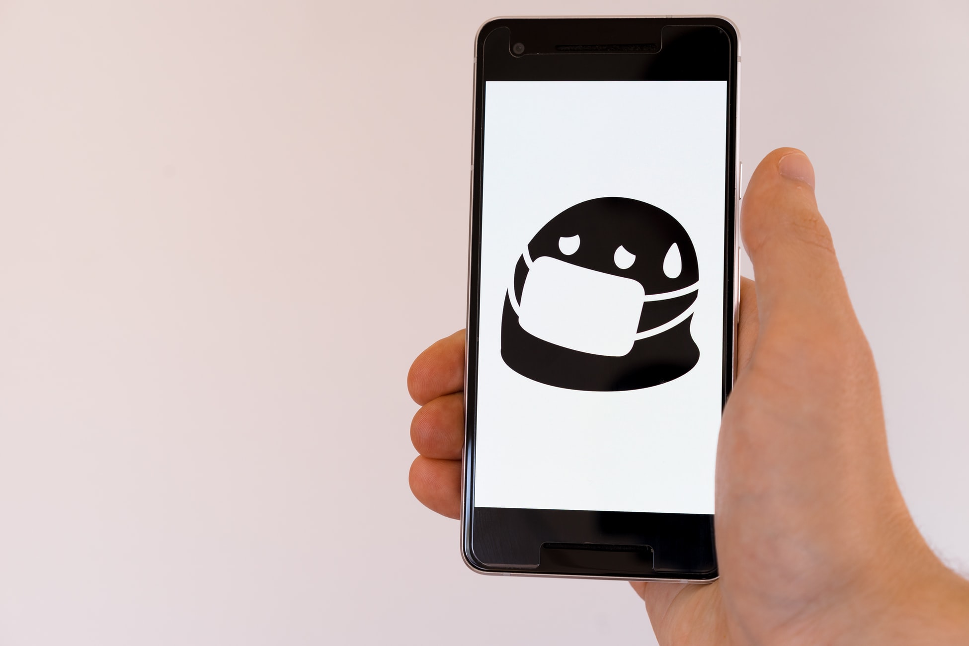 Shows a hand holding a mobile phone. The screen display is a cartoon face wearing a face mask