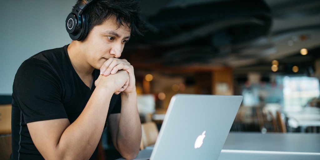 Young man learning online looking at computer screen and wearing headphones