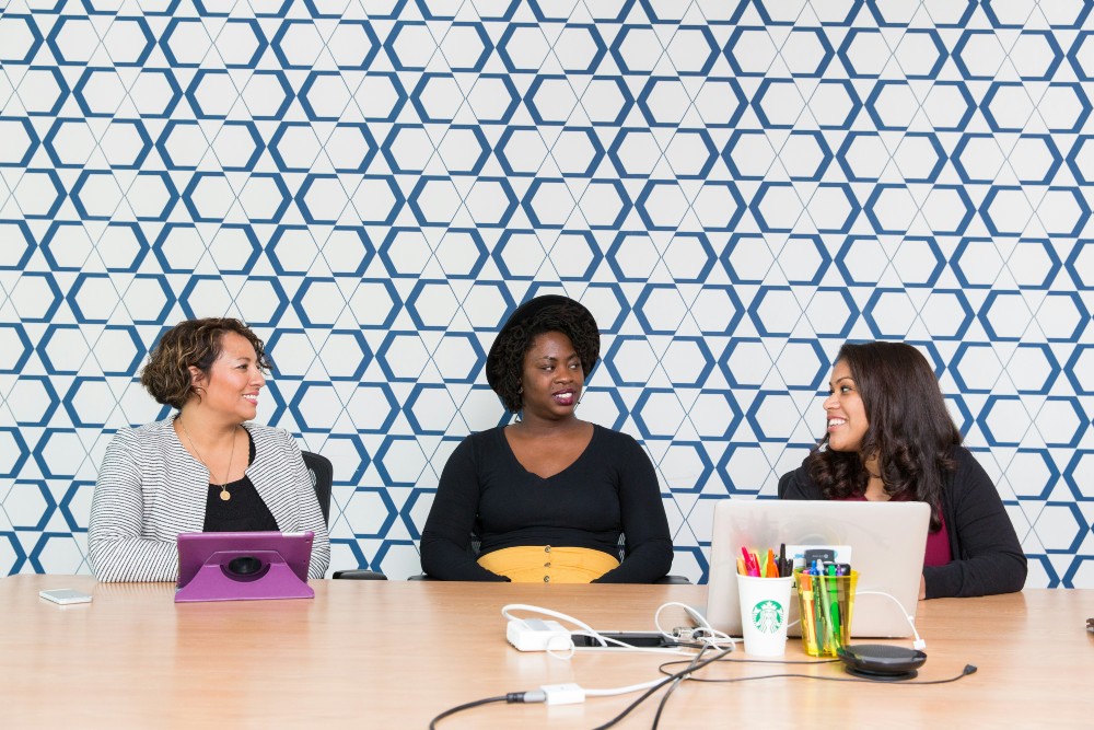 Group of three women sitting in front of patterned wall in workplace setting