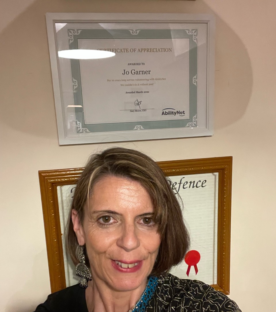 Jo Garner standing with her framed award on the wall above her head