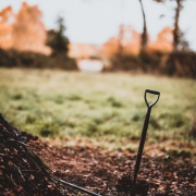 A garden spade stuck in the ground by a pile of leaves