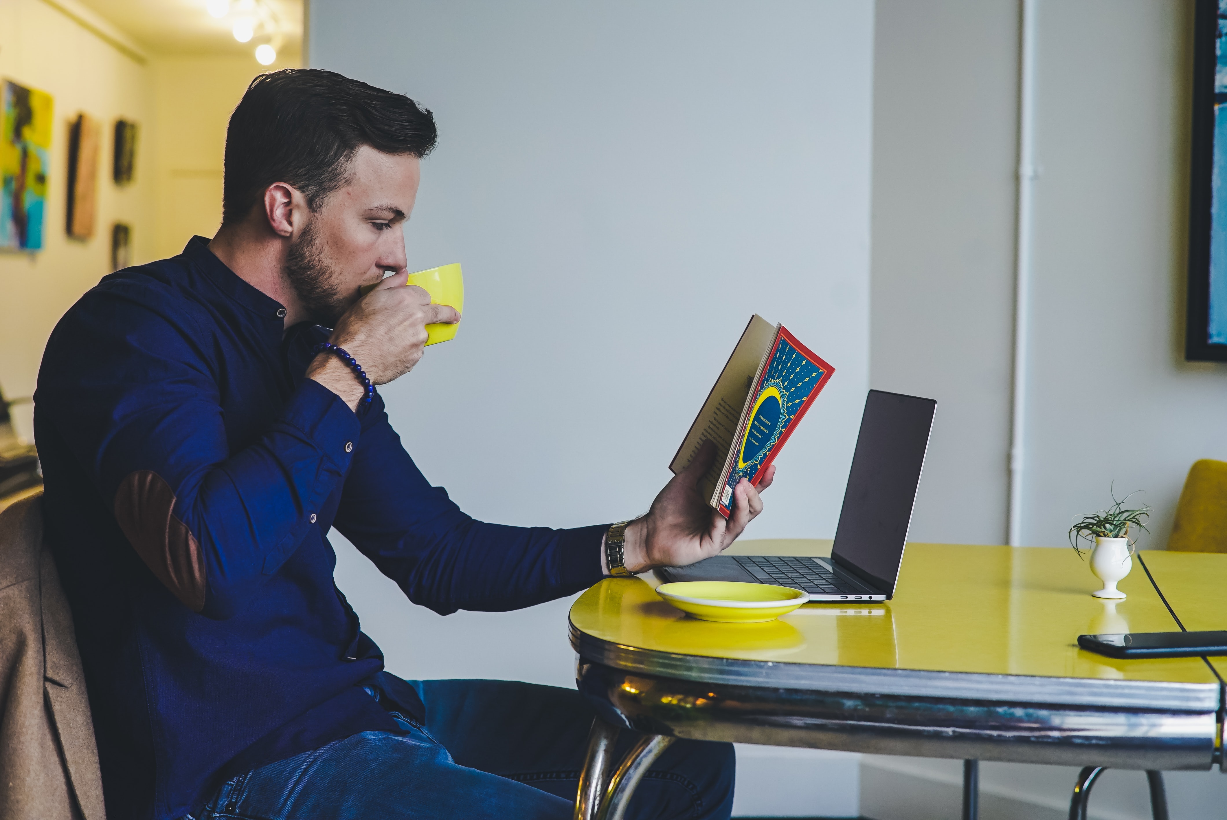 Man sitting at table with book, laptop and coffee