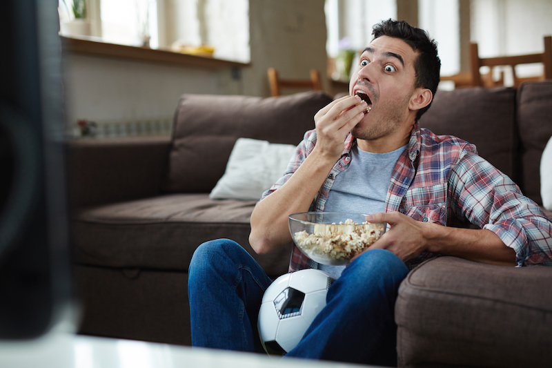 Man eating popcorn in front of TV looking surprised
