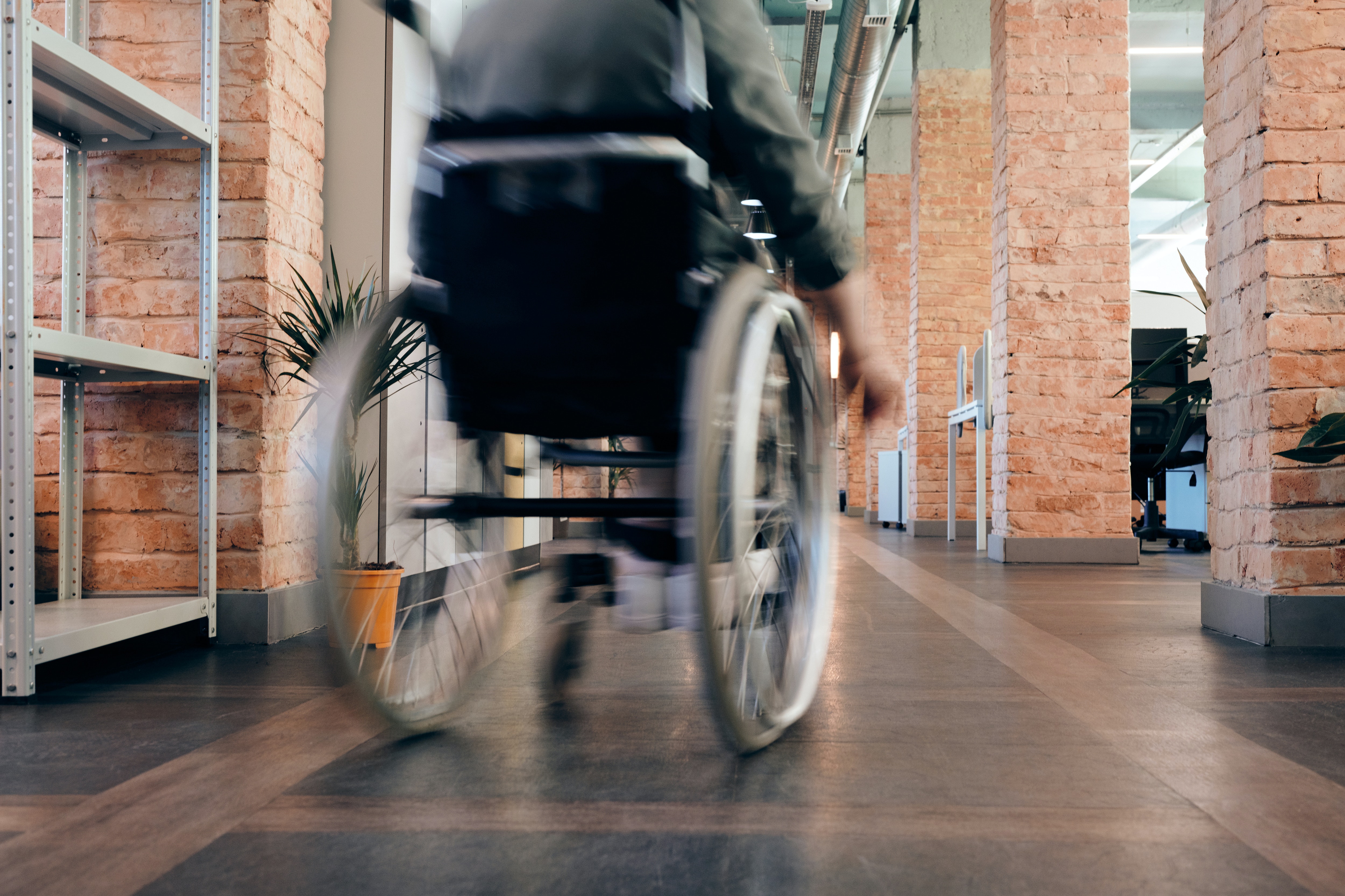 Image shows a man in a wheelchair moving around what appears to be an office. The image is slightly out of focus implying movement