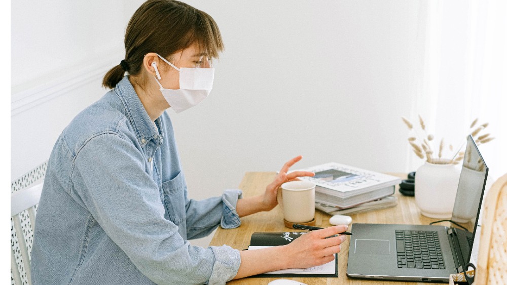 Person wearing face mask while working on laptop