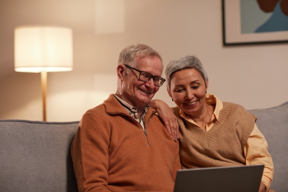 A couple smiling, sitting on sofa using laptop