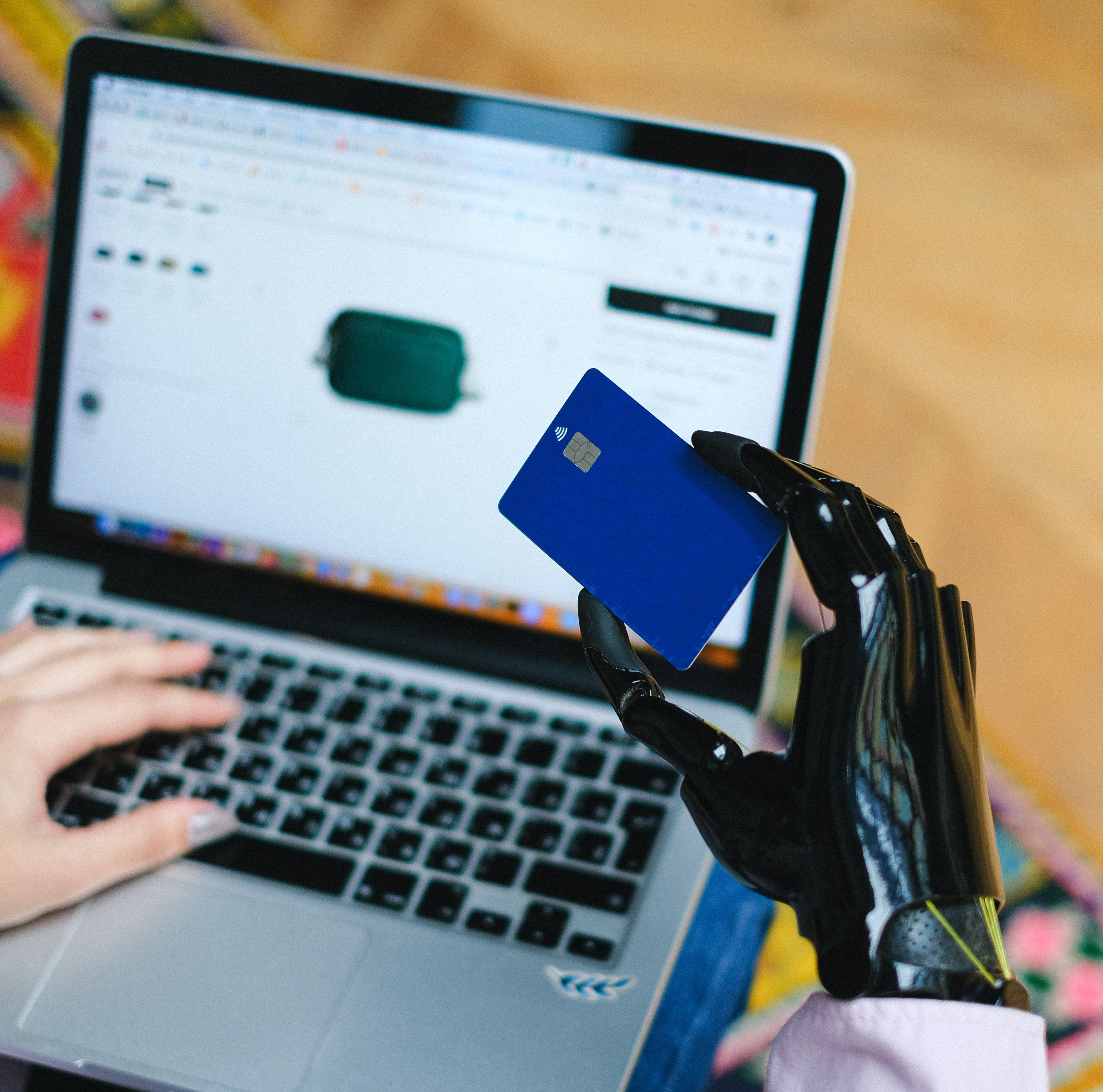 Image shows someone holding a credit card in front of a laptop screen. The hand is a prosthetic limb.