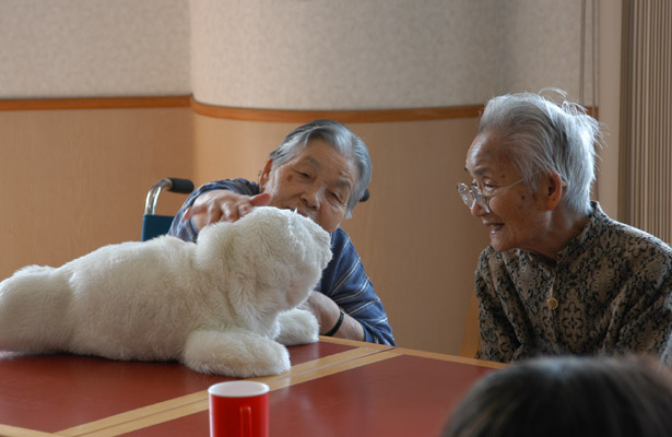 Image shows Japanese women at a tale stroking the robotic seal