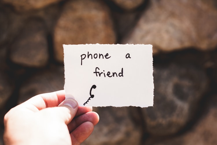 Shows a hand holding a piece of paper. On it are the words 'phone a friend'.
