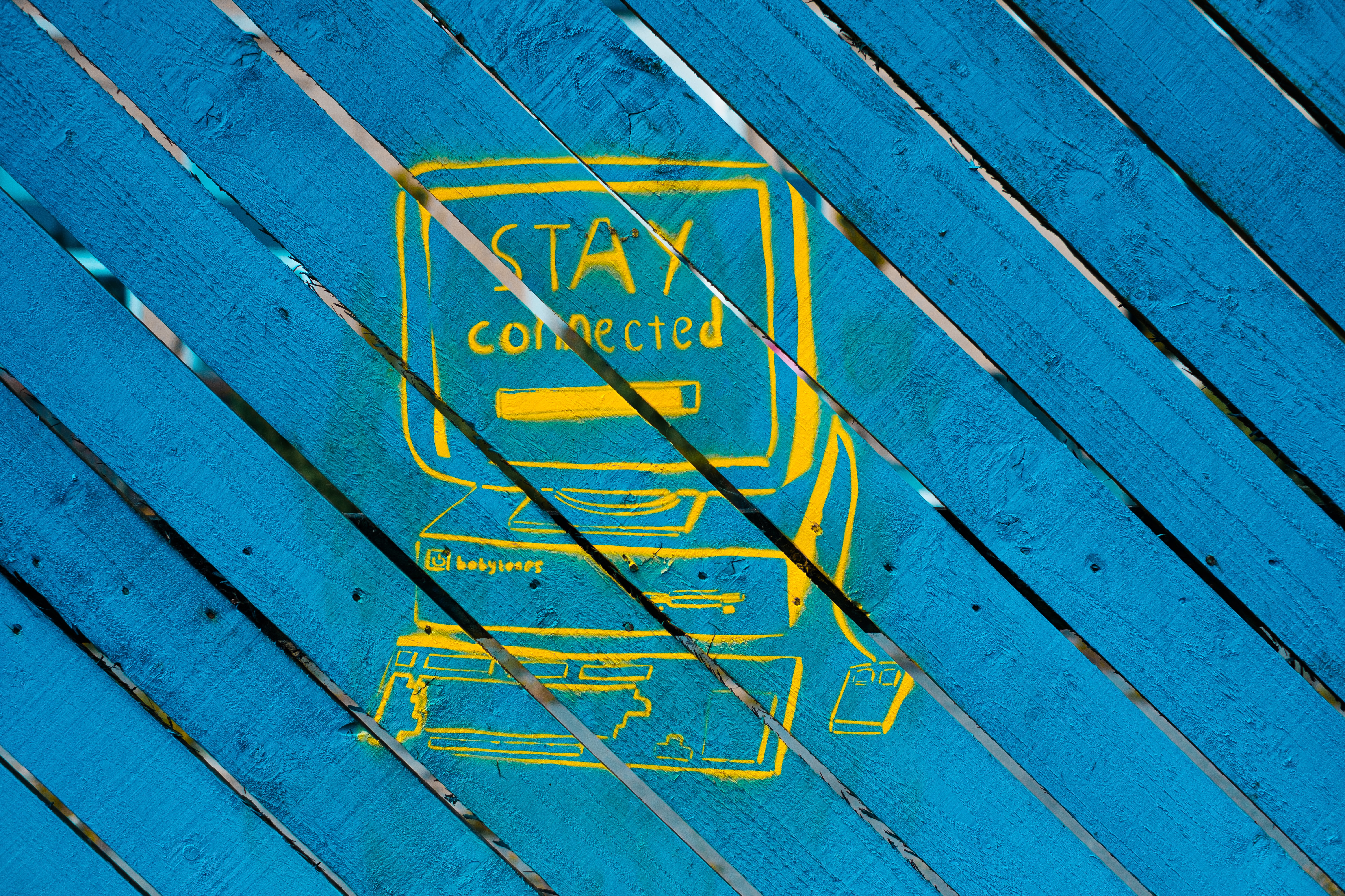 Images shows graffiti on a fence. Picture of a computer and the words "stay connected".