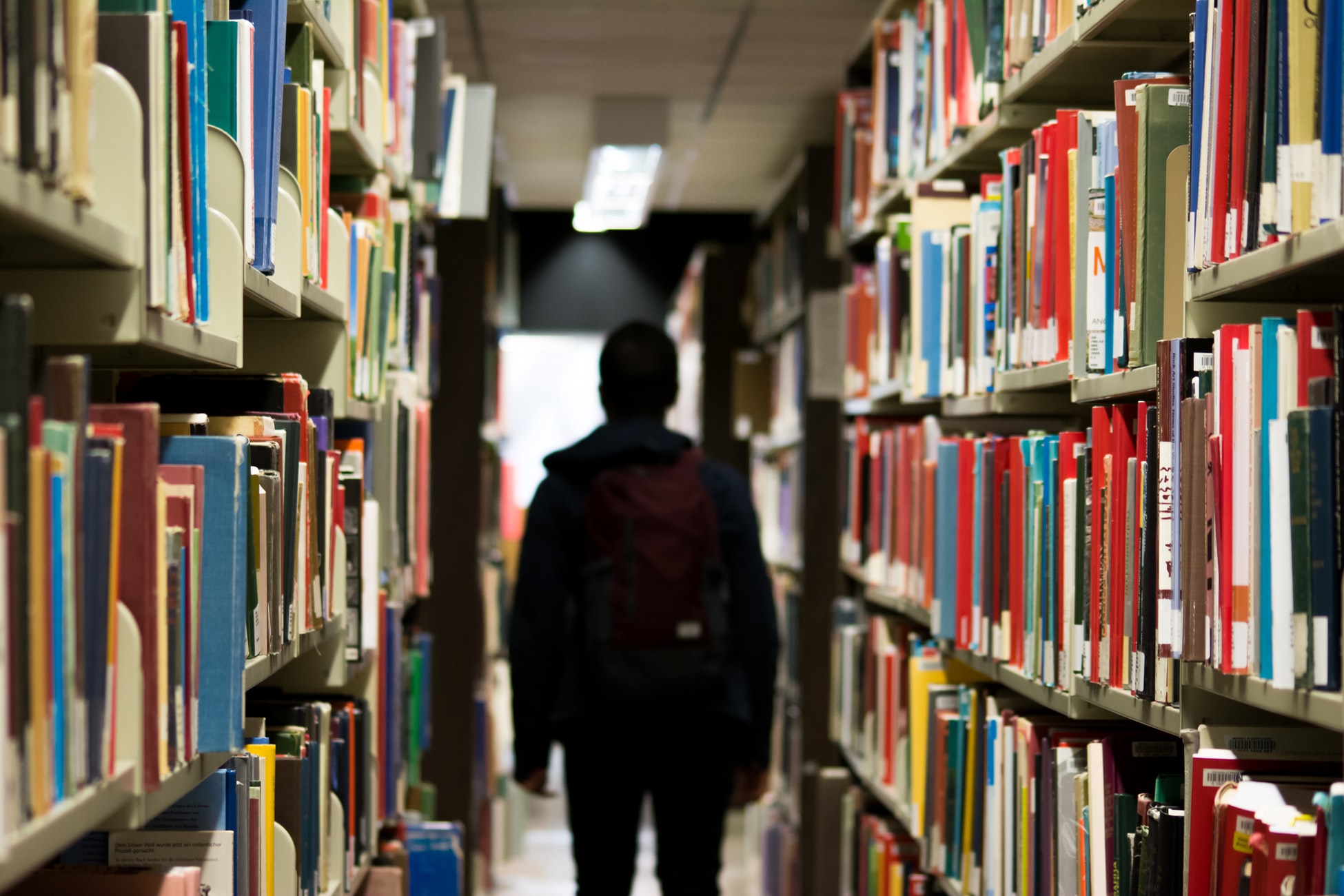 The silhouette of a young adult male walking between two shelves of books