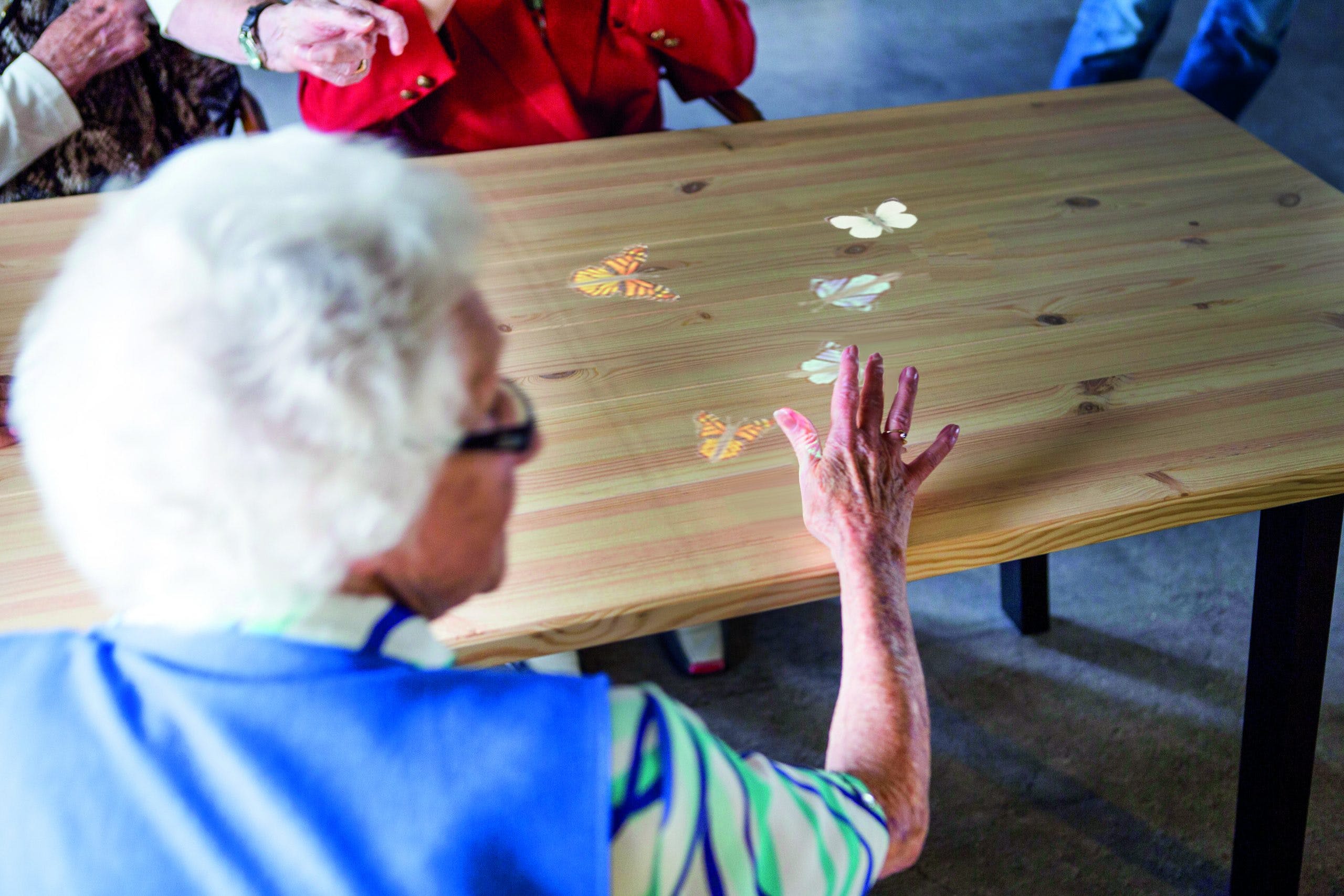 A picture of elderly people interacting with Tovertafel. Images of butterflies are projected onto a table.