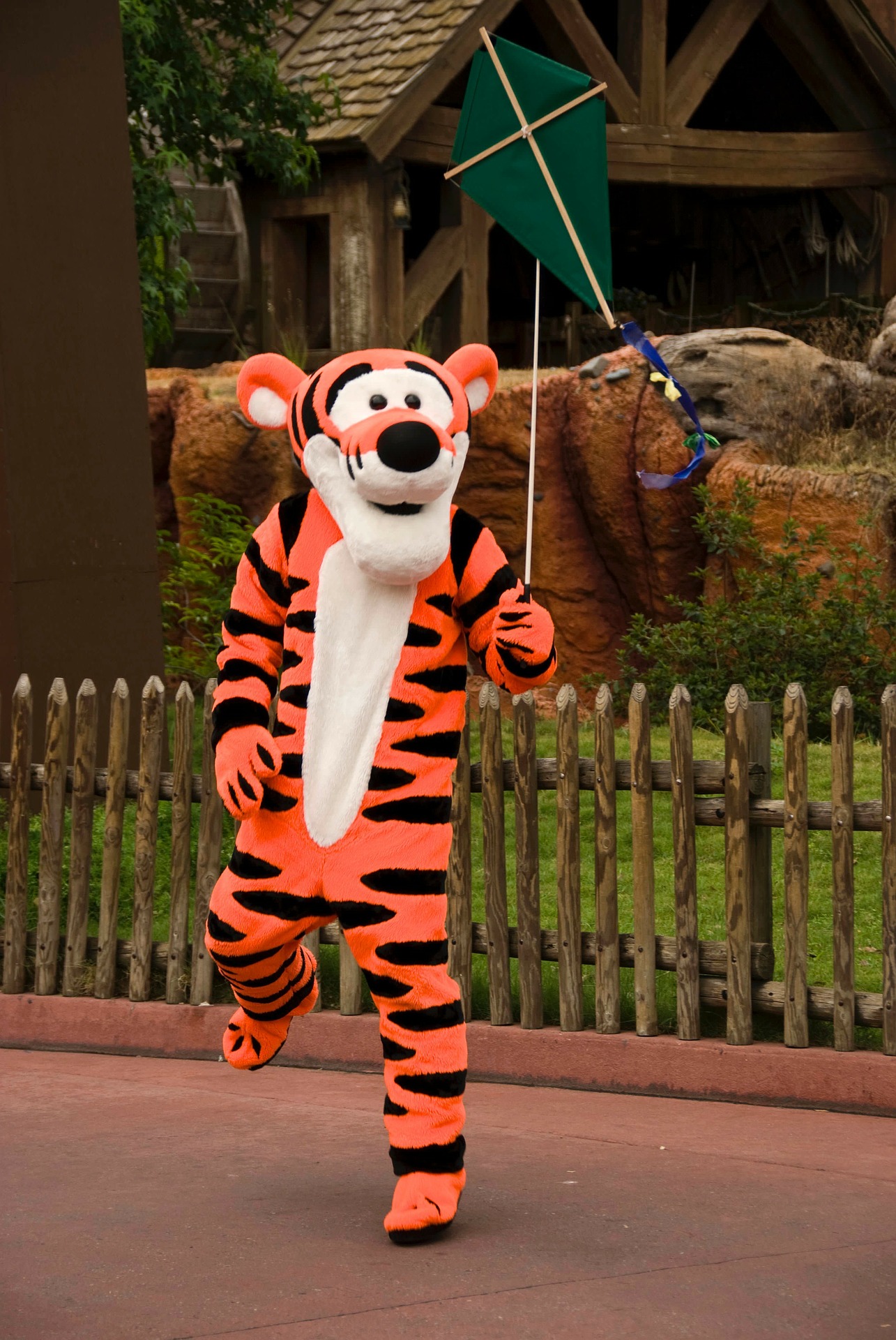 A photograph of someone in a Walt Disney Tigger outfit skipping with a kite