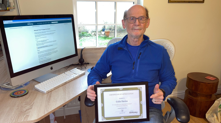 Colin Davies sitting at a desk holding a certificate for 10 years of service