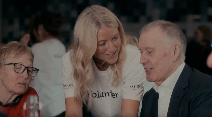 Geoff Hurst talks to an older lady using a digital device and a younger female BT volunteer